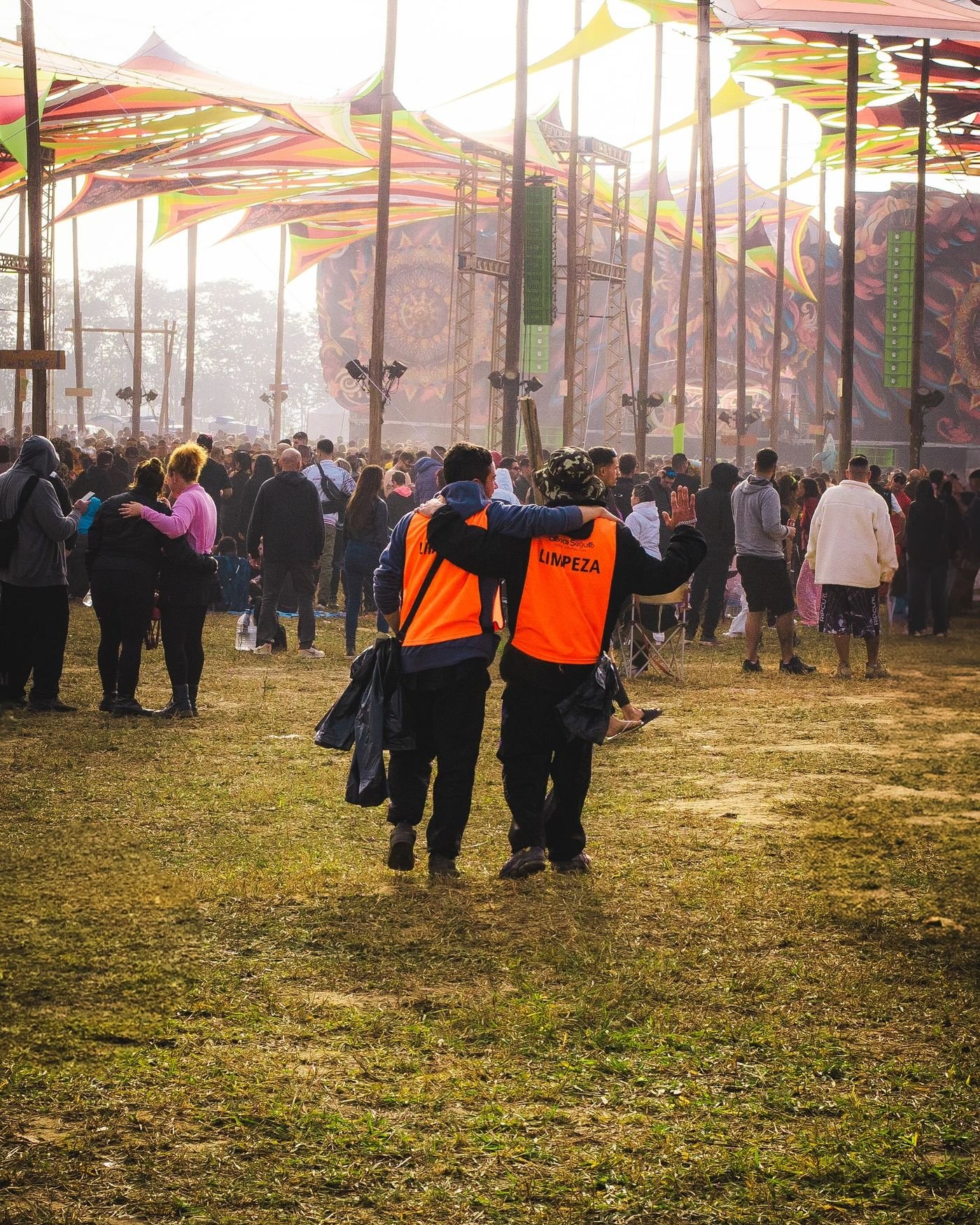 Dois Laranjinhas da Trance Segura, de colete laranja com LIMPEZA nas costas, caminhando juntos durante um festival